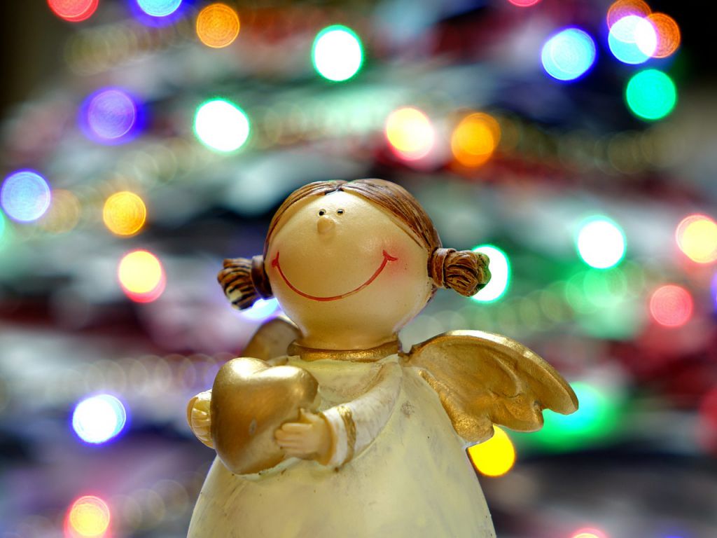 A figurine of a smiling angel, with a Christmas tree in the background.