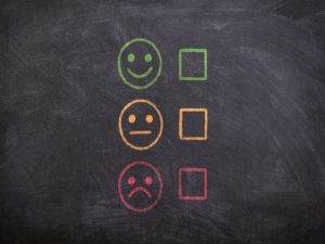 Three smiley faces with different emotions, next to empty tick boxes on a blackboard.