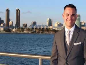 A businessman standing smiling with the San Diego skyline in the background.