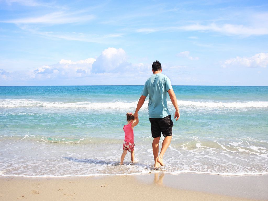 A daughter and a father walking on the beach, representing top East Coast cities for families.