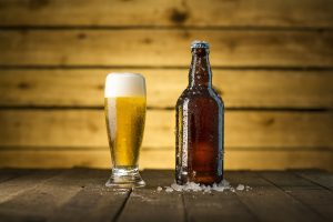 A beer bottle next to a glass of beer, against a wooden background.
