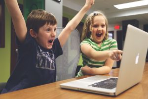 Two kids looking at a laptop and celebrating.