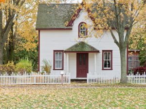 A suburban home surrounded by autumn trees, and a white picket fence.