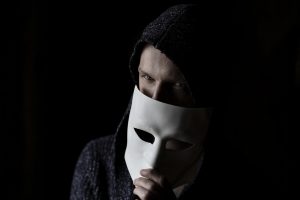 A scammer holding an Anonymous mask