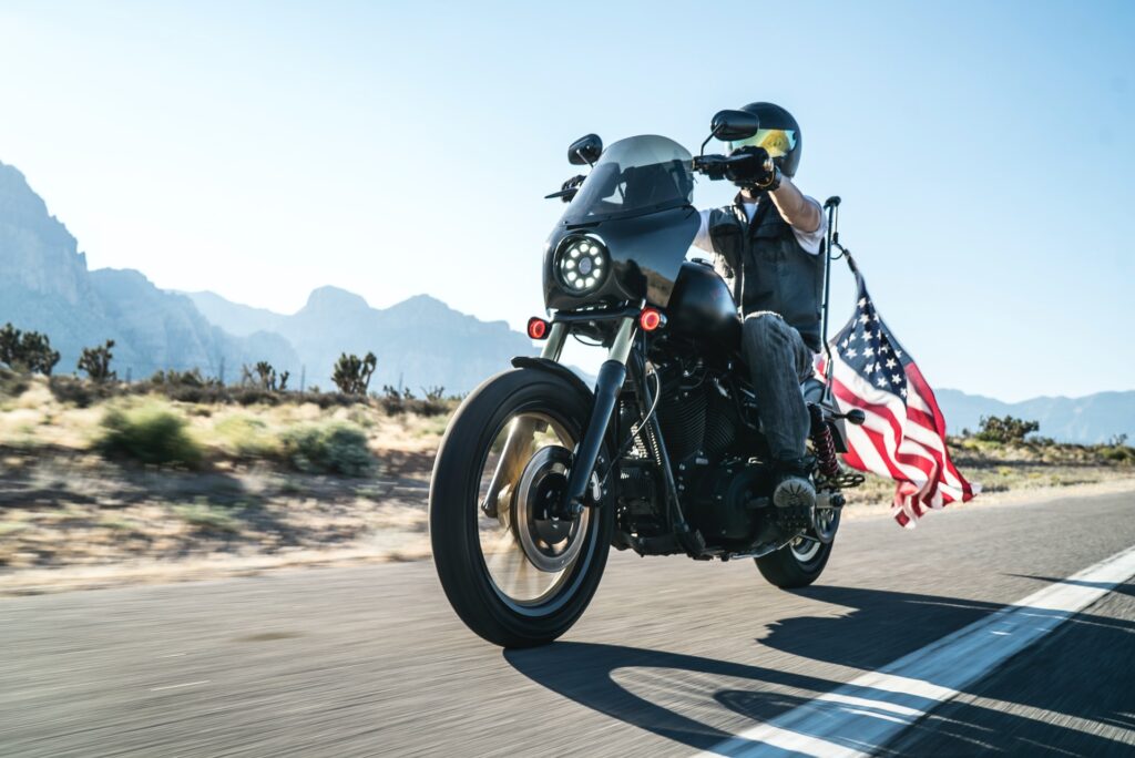 A man riding a motorcycle with an american flag behind him
