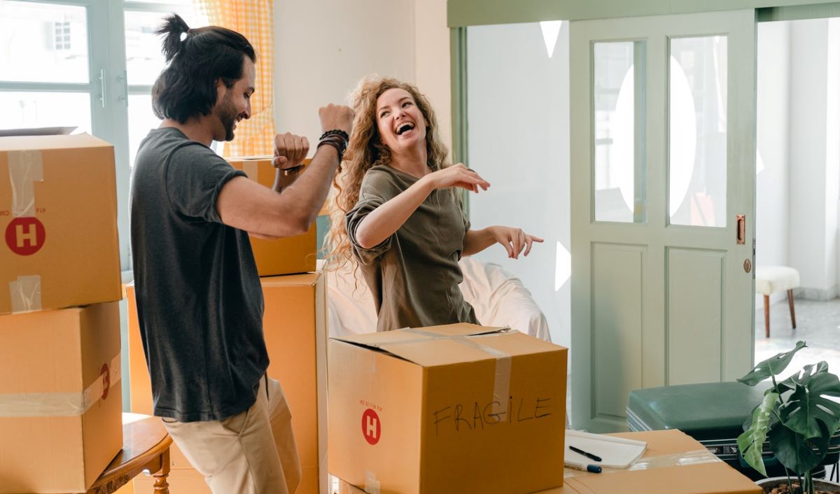 A happy couple dancing and having fun during packing because they managed to get discounts when moving.