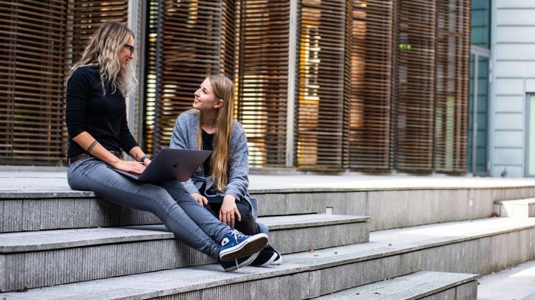 Two students sitting on the steps in front of university.