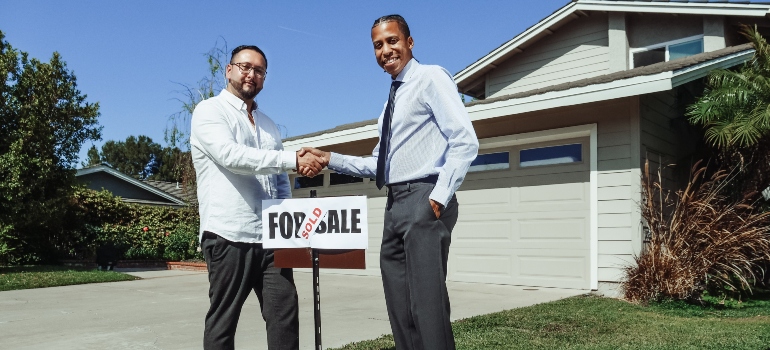 Two men shaking hands over the sign that says "sold".