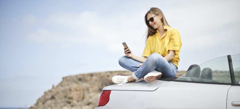 A woman sitting on the car and looking at her phone.