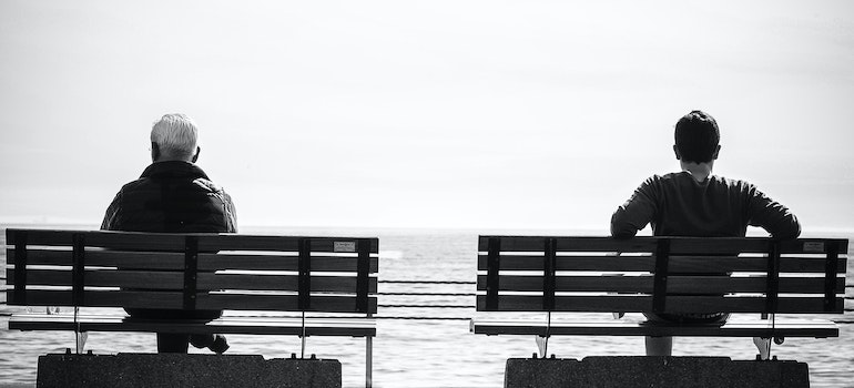 Two men sitting on separate benches at the coast.