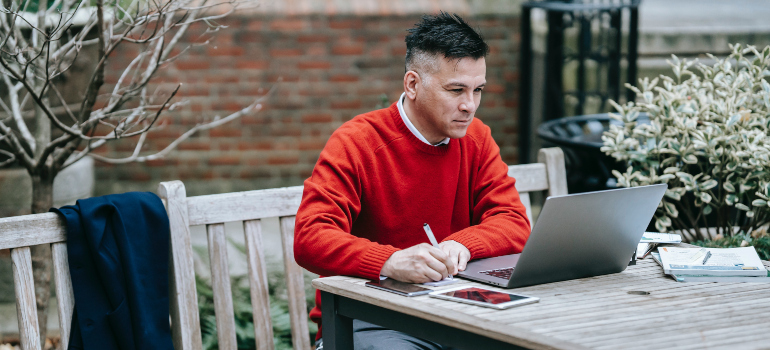 A man in a red sweater reading long distance moving companies Washington reviews on his laptop. 