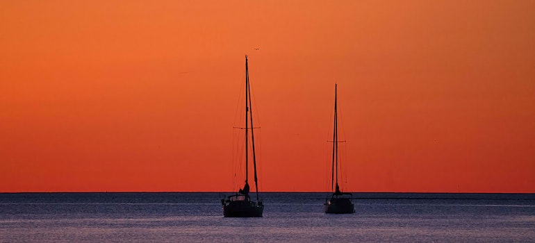 Two boats sailing during the sunset.