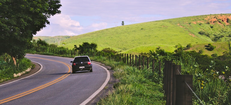 A car on the road next to a green hill.